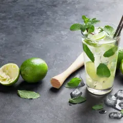 Orzeźwiający **mojito** z limonką i miętą, obok świeże limonki i kostki lodu.