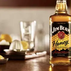 Butelka Jim Beam Honey na drewnianym blacie, obok cytryny i wyciskarki. Idealna na letnie wieczory.