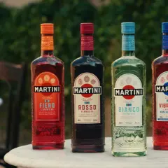 Pięć butelek Martini o różnych kolorach i smakach, stojących na stole na zewnątrz.