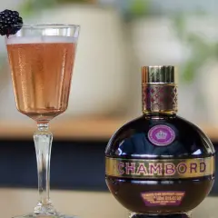 Elegancki kieliszek różowego drinka z jeżyną i butelka likieru Chambord.