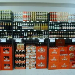 Półki sklepowe z piwem w butelkach i puszkach, w tym marki Warka, Żywiec i Dojlidy.