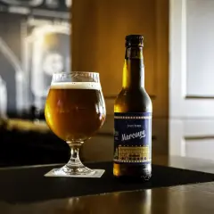 Szklanka pełna bursztynowego piwa marcowego obok butelki tego samego trunku.