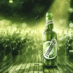 Zielona butelka piwa Tuborg Green na scenie, otoczona tłumem innych butelek. W tle mikrofon.
