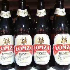 Rząd butelek piwa Łomża Export Pszeniczne. Etykiety ozdobione postaciami w strojach ludowych.