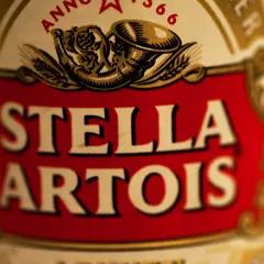 Zbliżenie na etykietę piwa Stella Artois. Czerwone tło z białym napisem.