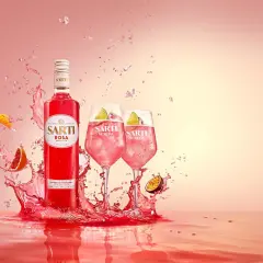 Sarti Rosa Aperitivo i dwa drinki Sarti Spritz z lodem i limonką, otoczone eksplozją owoców i różowego płynu.