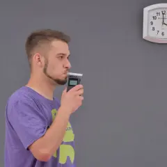 Mężczyzna dmucha w alkomat, obok wisi zegar.