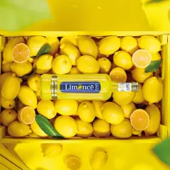 Butelka Limoncé Spritz leżąca w skrzynce pełnej cytryn.