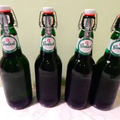 Cztery butelki piwa Grolsch z charakterystycznymi zamknięciami typu swing-top, stojące obok siebie.