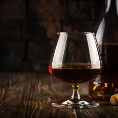 Kieliszek z bursztynowym brandy Stock 84 i butelka na drewnianym stole.