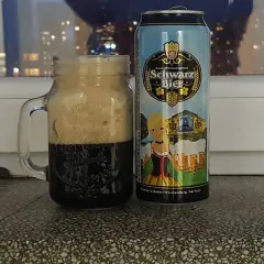 Perlenbacher Schwarz Bier w kuflu, obok puszka piwa. W tle nocne światła miasta.