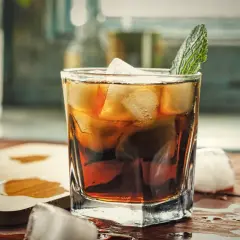 Orzeźwiający gin z colą, z kostkami lodu i listkiem mięty, na drewnianym blacie.