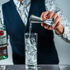 Barman nalewa rum z butelki Bacardi do szklanki z lodem, przygotowując drinka rum z colą.