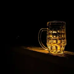 Złocisty kufel piwa Grimbergen, podświetlony od tyłu, stoi na kamiennym murku w ciemności.