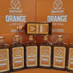 Jägermeister Orange, jeden z rodzajów Jägermeister, w butelkach i kartonach, z pomarańczowym motywem.