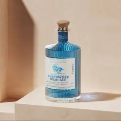 Niebieska butelka ginu Drumshanbo Gunpowder Irish Gin, inspirowanego podróżami do Bombaju, z drewnianym korkiem i etykietą z jeleniem.