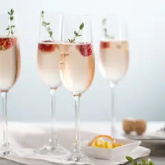 Cztery kieliszki orzeźwiającego prosecco rose z malinami i gałązkami tymianku, gotowe na toast.