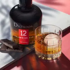 Butelka rumu Dictador 12 Years Colombian Rum obok szklanki z drinkiem i kawałków czekolady.