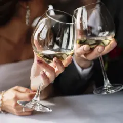 Para młoda wznosi kieliszki z białym winem na weselu.
