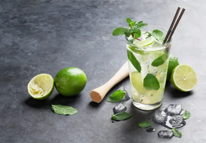 Orzeźwiający **mojito** z limonką i miętą, obok świeże limonki i kostki lodu.