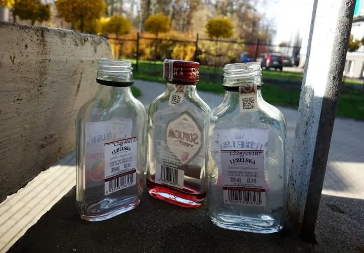 Trzy puste butelki po alkoholu, w tym jedna z czerwonym płynem, leżą na betonowym murku. Małpka alkoholowa, symbol beztroski, ale i problemu.