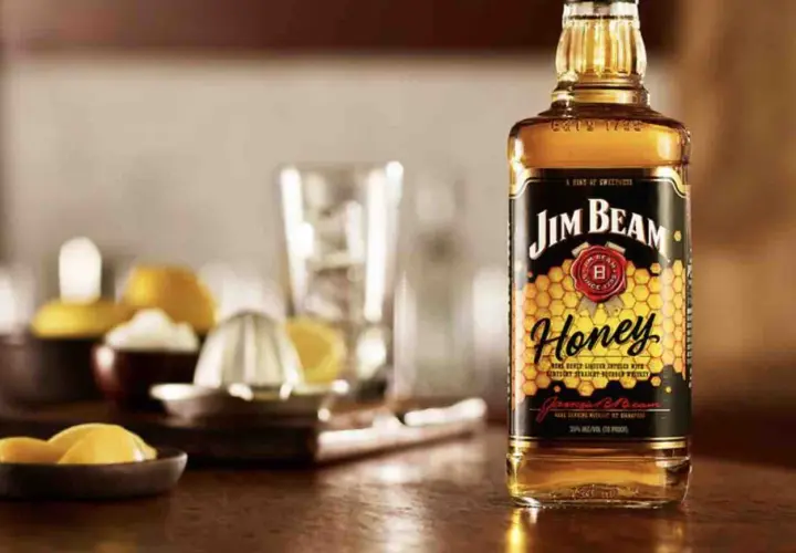Butelka Jim Beam Honey na drewnianym blacie, obok cytryny i wyciskarki. Idealna na letnie wieczory.