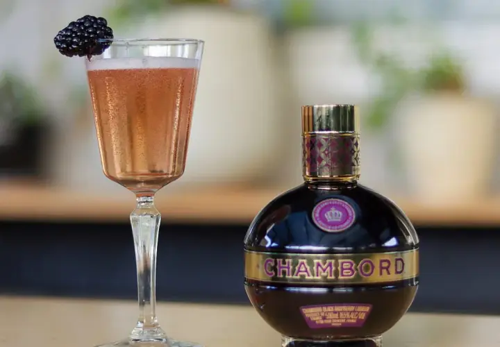 Elegancki kieliszek różowego drinka z jeżyną i butelka likieru Chambord.