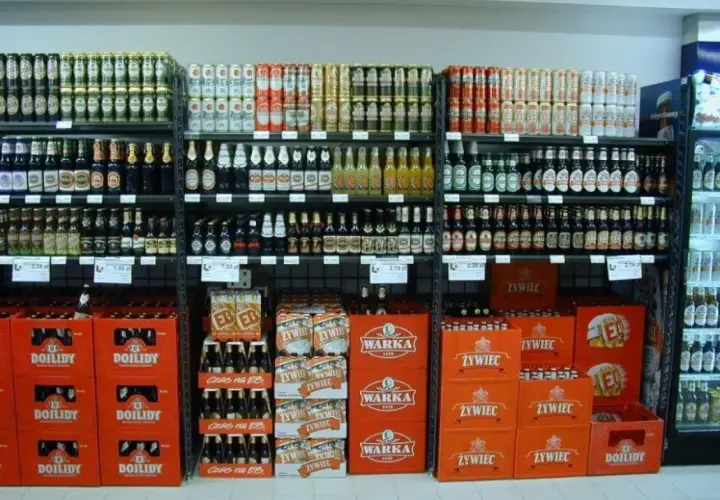Półki sklepowe z piwem w butelkach i puszkach, w tym marki Warka, Żywiec i Dojlidy.