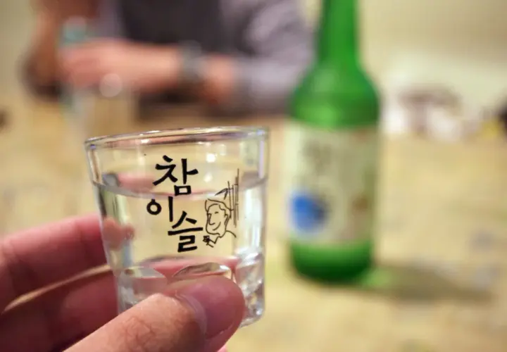 Szklaneczka z soju, na której widnieje napis "참이슬" i rysunek. Zastanawiasz się, soju ile procent?