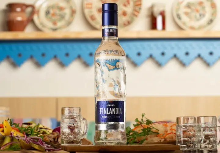 Butelka wódki Finlandia z kieliszkami i przekąskami na stole.