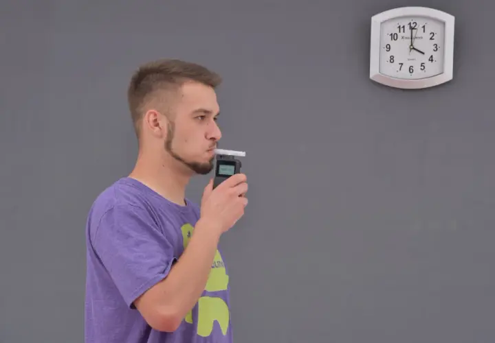 Mężczyzna dmucha w alkomat, obok wisi zegar.