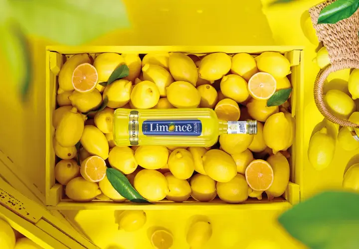 Butelka Limoncé Spritz leżąca w skrzynce pełnej cytryn.