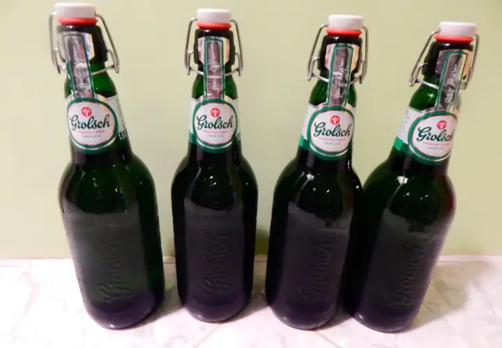 Cztery butelki piwa Grolsch z charakterystycznymi zamknięciami typu swing-top, stojące obok siebie.