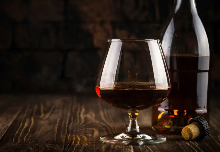 Kieliszek z bursztynowym brandy Stock 84 i butelka na drewnianym stole.