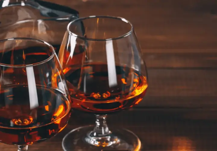 Dwa kieliszki z bursztynowym koniakiem i karafka na drewnianym stole. Idealny wieczór z brandy.