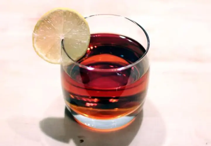 Szklanka z ciemnoczerwonym Martini Rosso, ozdobiona plasterkiem cytryny, stoi na jasnym blacie.