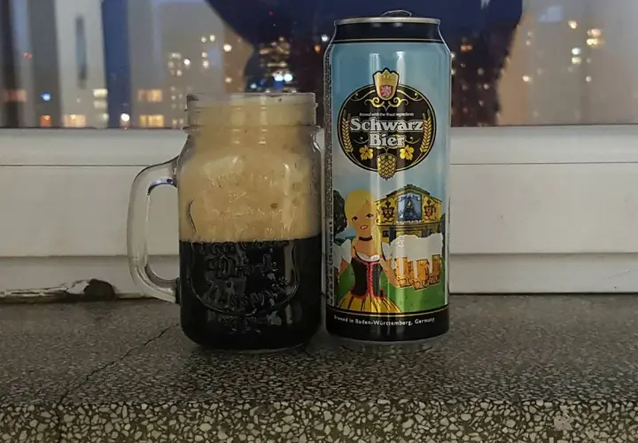 Perlenbacher Schwarz Bier w kuflu, obok puszka piwa. W tle nocne światła miasta.