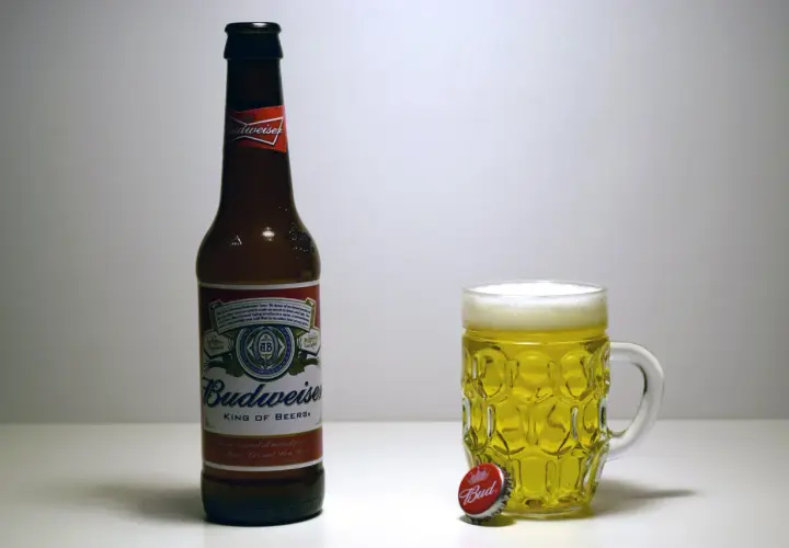 Butelka i kufel pełne złotego piwa Budweiser. Obok leży kapsel z napisem "Bud".