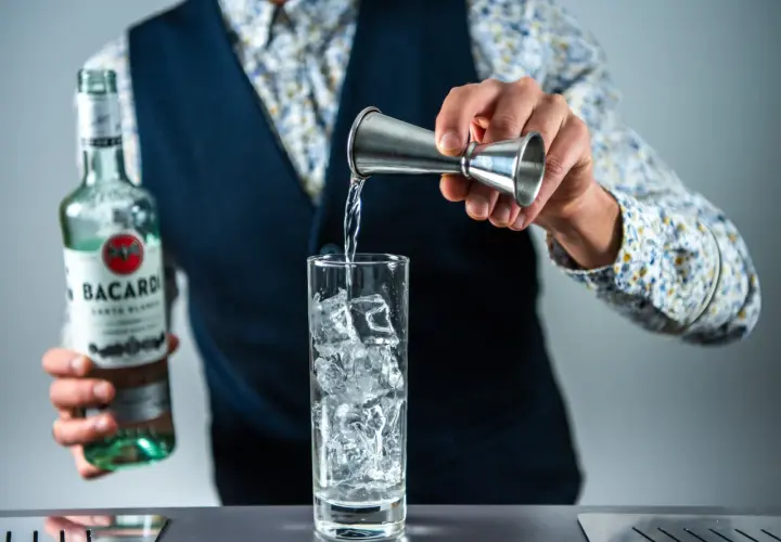 Barman nalewa rum z butelki Bacardi do szklanki z lodem, przygotowując drinka rum z colą.