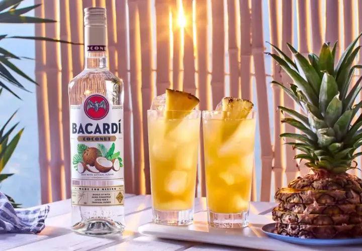 Butelka Bacardi Coconut obok dwóch drinków z ananasem i cała ananasowa piramidka. Idealne na tropikalne przyjęcie!