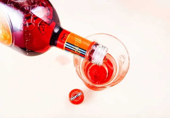 Czerwony Martini Fiero nalewany do kieliszka. Obok leży czerwona zakrętka z logo Martini.