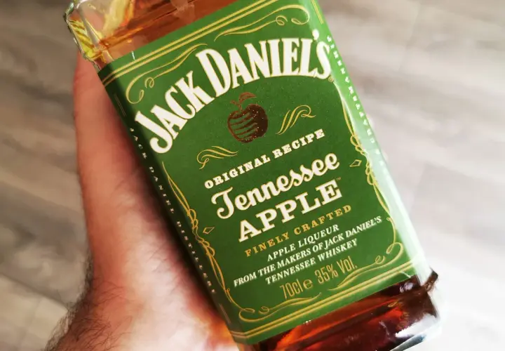Dłoń trzyma butelkę Jack Daniel's Tennessee Apple. Ten miodowy likier jabłkowy to idealny dodatek do wieczoru.