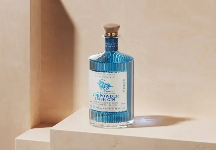 Niebieska butelka ginu Drumshanbo Gunpowder Irish Gin, inspirowanego podróżami do Bombaju, z drewnianym korkiem i etykietą z jeleniem.