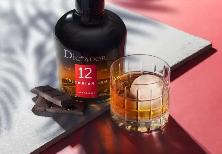 Butelka rumu Dictador 12 Years Colombian Rum obok szklanki z drinkiem i kawałków czekolady.