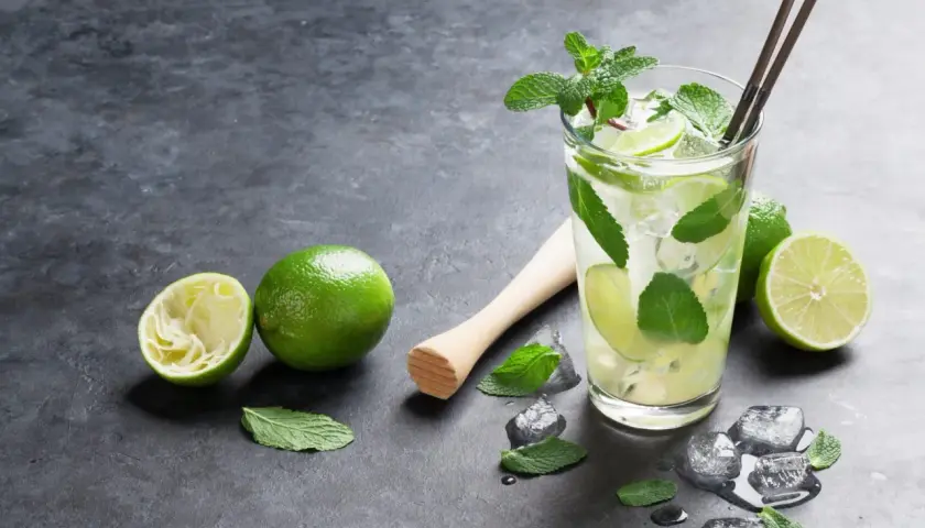 Orzeźwiający **mojito** z limonką i miętą, obok świeże limonki i kostki lodu.