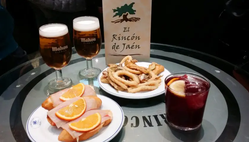 Dwa piwa Mahou, tapas z szynką i pomarańczą, smażone kalmary i sangria na stole w El Rincón de Jaén.