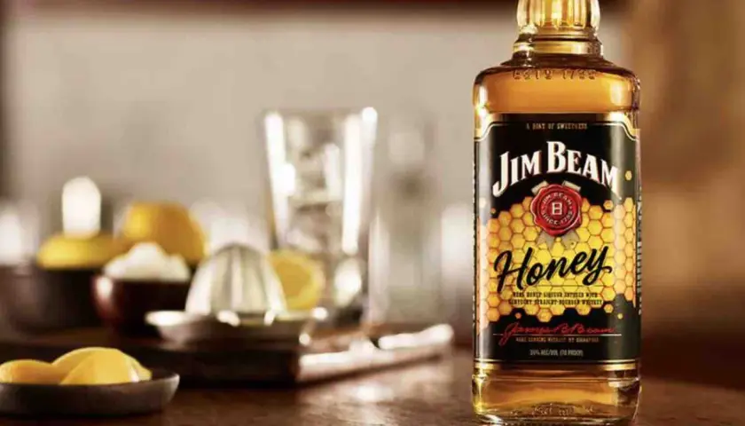 Butelka Jim Beam Honey na drewnianym blacie, obok cytryny i wyciskarki. Idealna na letnie wieczory.