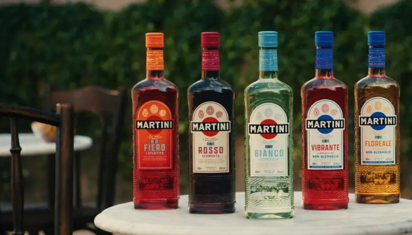 Pięć butelek Martini o różnych kolorach i smakach, stojących na stole na zewnątrz.