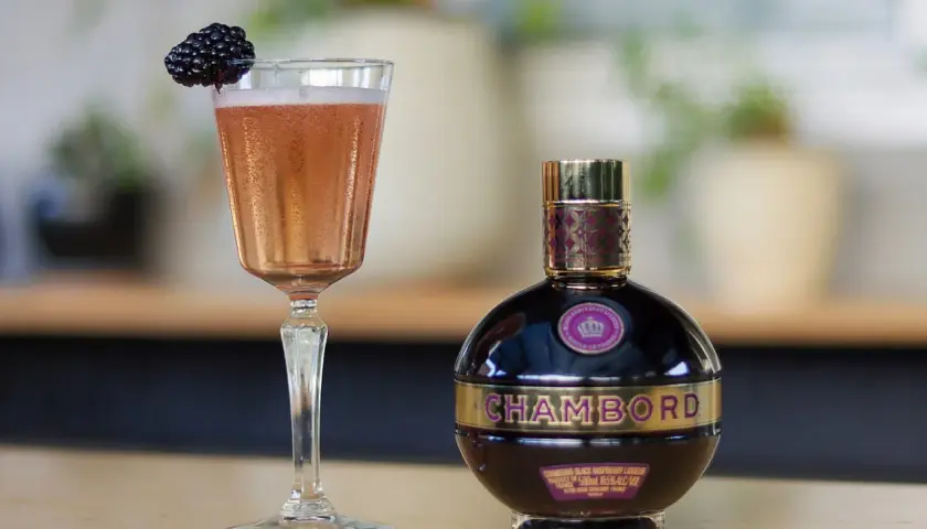 Elegancki kieliszek różowego drinka z jeżyną i butelka likieru Chambord.