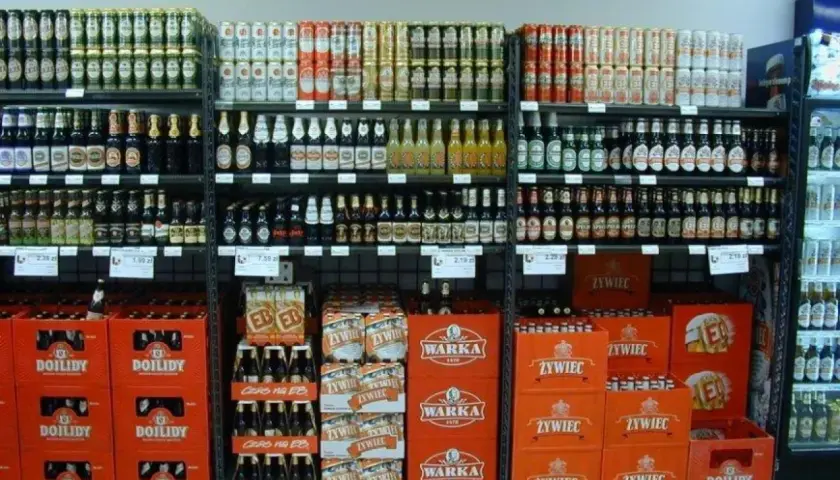 Półki sklepowe z piwem w butelkach i puszkach, w tym marki Warka, Żywiec i Dojlidy.